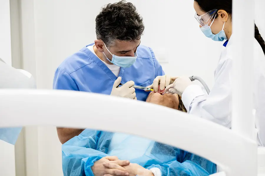 A surgeon and an assistant at the chair, the patient’s hands folded