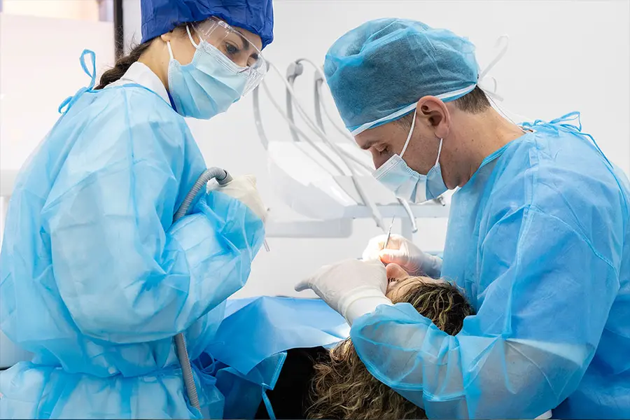 An assistant with the suction and a clinician leaning over the patient