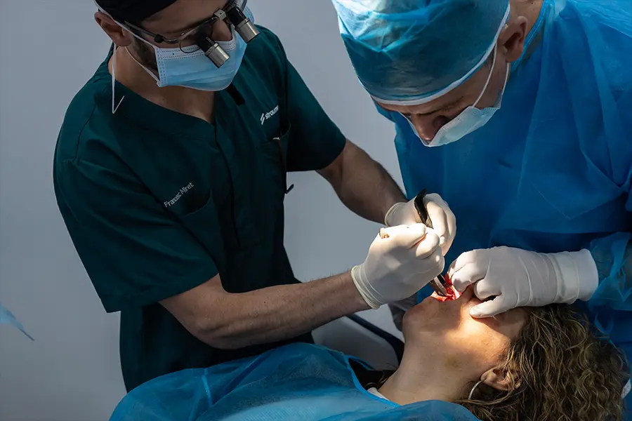 A clinician in green scrubs and another with loupes operating together