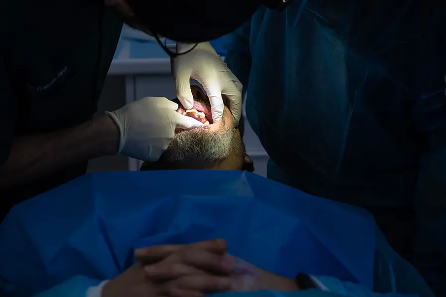 A surgeon’s gloved hands operating in the mouth, the patient draped in blue