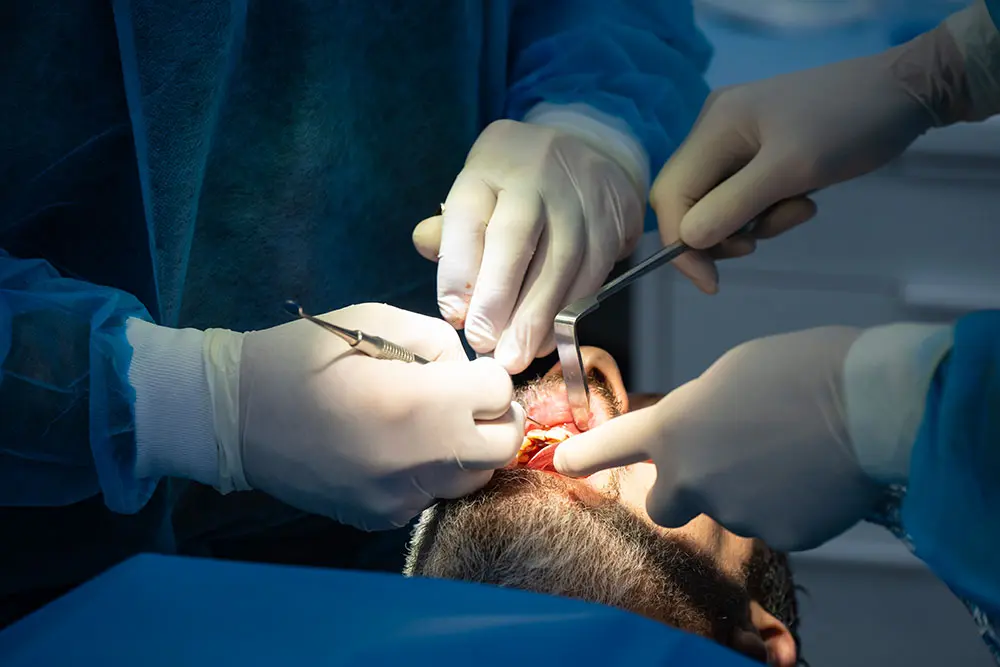 Two pairs of gloved hands operating in the mouth, seen close up
