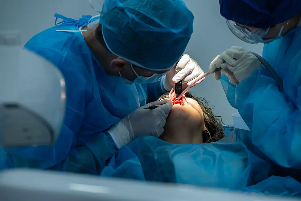 A surgeon wearing loupes and an assistant working inside the patient’s mouth